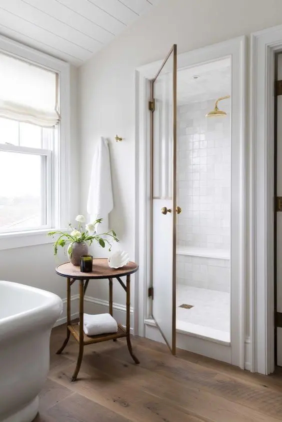 a modern elegant bathroom in neutrals, with a hardwood floor, a large shower space clad with white tiles and a wooden side table