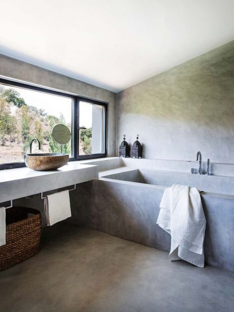 a modern ethnic bathroom with concrete walls and a floor, a bathtub and a floating vanity, a basket for storage and a sink