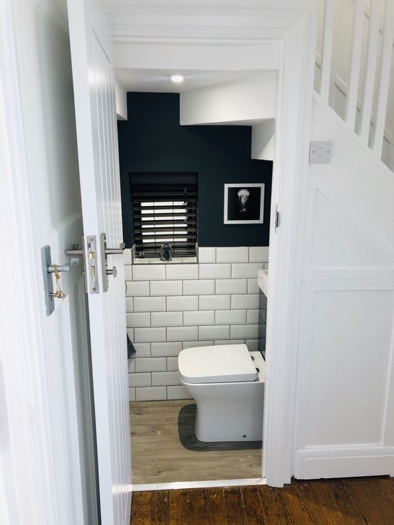a modern under stair powder room with navy walls and white subway tiles, white appliances and an artwork is a stylish and contrasting idea