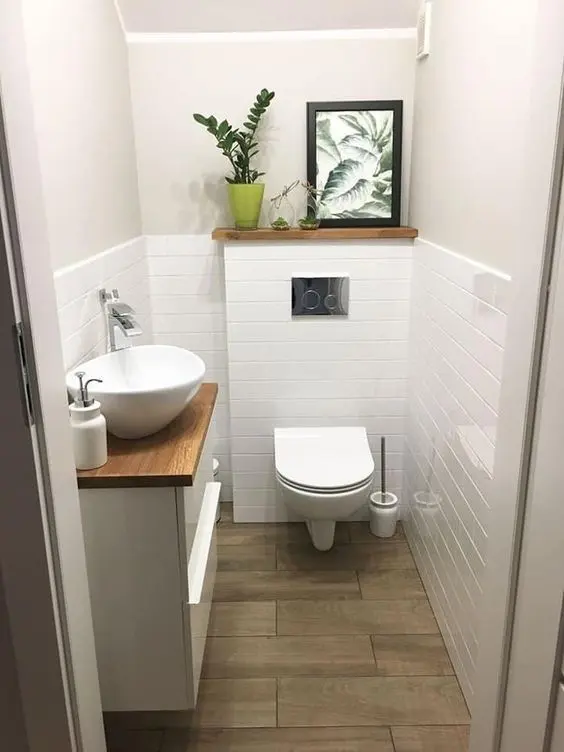 a modern white powder room under the stairs with white tiles, a white vanity with a bowl sink and some cool decor