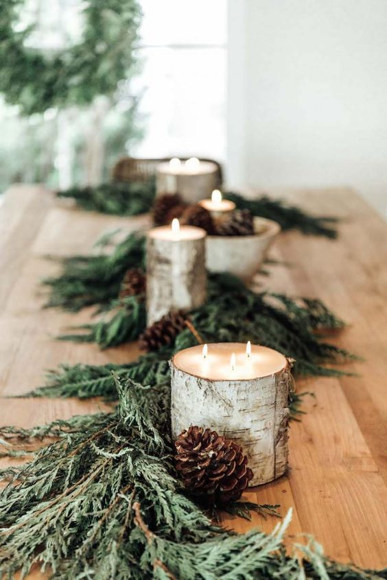 a natural woodland Christmas tablescape with evergreens, pinecones and candles wrapped with birch