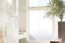 a neutral and welcoming shower space with a frosted glass window and white marble tiles all over