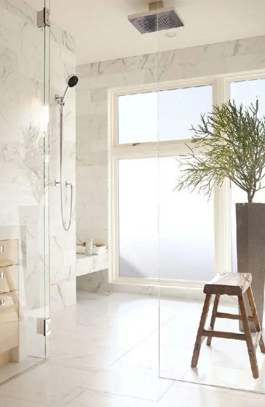 a neutral and welcoming shower space with a frosted glass window and white marble tiles all over