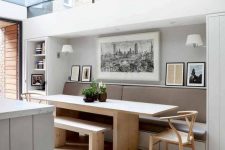 a neutral modern dining space with a grey leather banquette, a long light-stained table, a bench and chairs plus some artworks