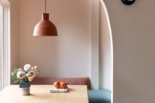 a pastel dining space with an arch, a pastel banquette seating, a matching upholstered bench, a pendant lamp and a window