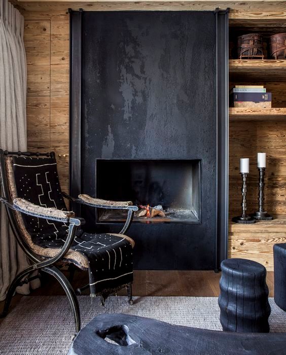 a pretty space with plywood covering all the walls, a fireplace clad with aged black metal a catchy vintage chair and black side tables