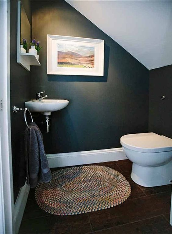 a pretty under the stairs powder room with black walls, a little wall-mounted sink, a colorful rug and some cool decor