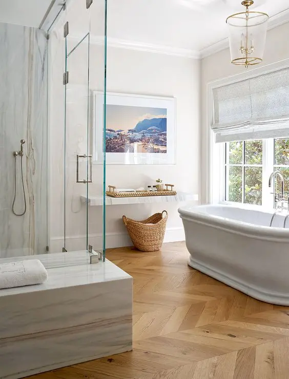 a refined bathroom done with a light-stained parquet floor and white stone slabs, a chic tub and some windows is very welcoming