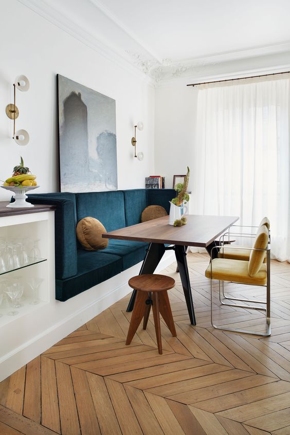 a refined dining area with a navy banquette, a chic table, yellow chairs and wooden stools plus a storage niche