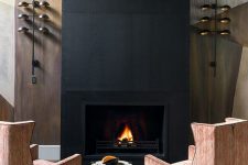 a refined fireplace nook with a fireplace clad with black metal, striped chairs, a tiny side table and cool wall lamps