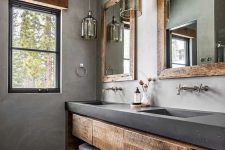 a rustic bathroom with concrete walls, a pebble floor, a rough wood vanity with a concrete countertop, pendant lamps and mirrors
