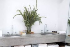 a rustic bathroom with white walls, a concrete floating vanity with a wooden shelf, a basket for storage and some greenery