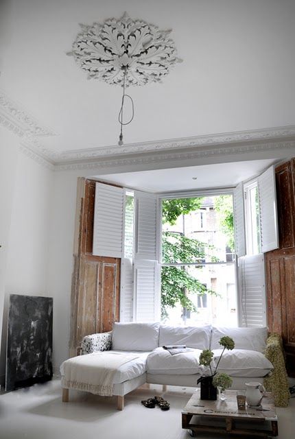 a shabby chic space with beautiful vintage crown molding and a matching medallion, a white sectional and modern and vintage shutters is light filled