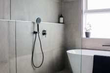 a simple contemporary bathroom with concrete tiles on the walls and floor, an oval tub, black fixtures and a window