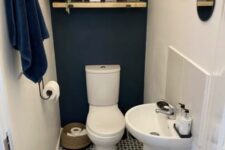 a small and cool under the stairs powder room with a navy accent wall, a printed floor, an open shelf with decor and a free-standing sink looks stylish