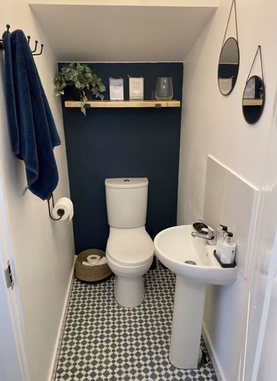 a small and cool under the stairs powder room with a navy accent wall, a printed floor, an open shelf with decor and a free-standing sink looks stylish