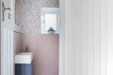 a small and pretty under stair powder room with pink chevron tiles, speckle wallpaper, a blue floating vanity and a small sink