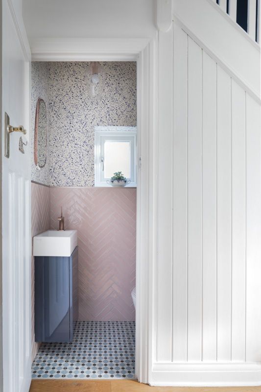 a small and pretty under stair powder room with pink chevron tiles, speckle wallpaper, a blue floating vanity and a small sink
