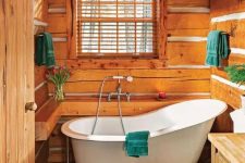 a small cabin bathroom clad with wood, with wooden beams, a wooden vanity, a clawfoot tub and bold textiles