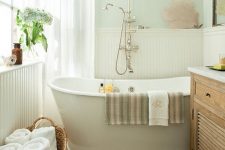 a small modern bathroom with pastel walls and white planks, a hardwood floor, an oval tub and vintage fixtures for more chic
