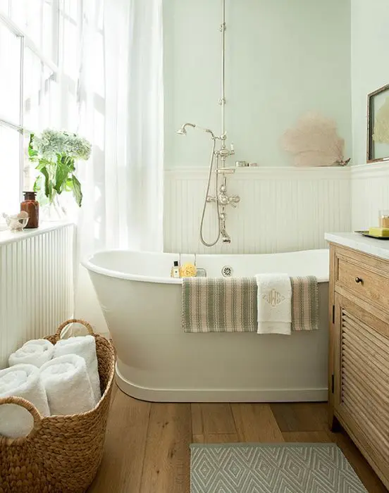 a small modern bathroom with pastel walls and white planks, a hardwood floor, an oval tub and vintage fixtures for more chic
