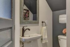 a small modern powder room with a grey accent wlal, printed tile on the floor, a wall-mounted sink and a mirror with a shabby chic frame