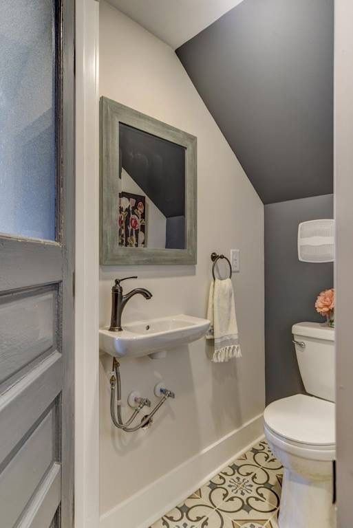 a small modern powder room with a grey accent wlal, printed tile on the floor, a wall-mounted sink and a mirror with a shabby chic frame