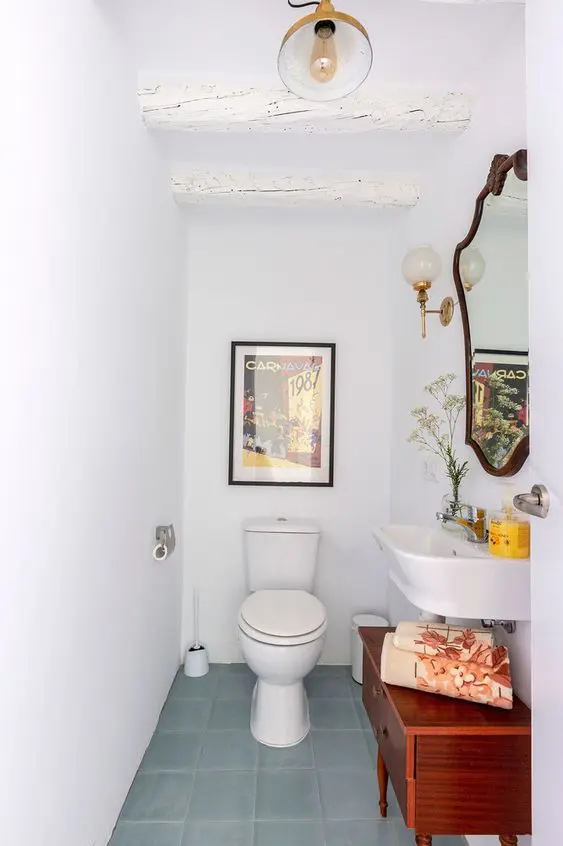 a small powder room under the staircase with a wall-mounted sink, a stained cabinet, whitewashed beams, a mirror in a vintage frame