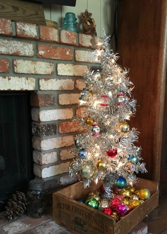 a small silver Christmas tree with colorful vintage ornaments placed into a tray with such ornaments