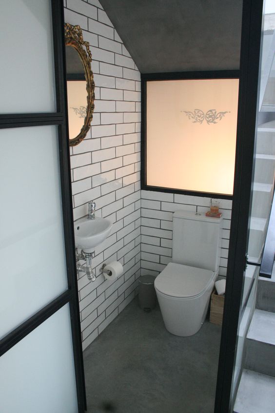 a  small under stair guest toilet clad with white tiles, with a faux window, white appliances and a mirror in an ornated frame