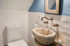 a small under the stairs powder room with a blue accent wall, white brick clad and tiles, a wall-mounted sink, a mirror and a toilet