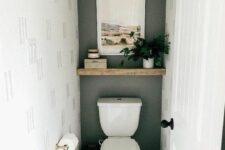 a small under the stairs powder room with a grey accent wall, a wooden shelf with decor and a toilet plus a marble tile floor