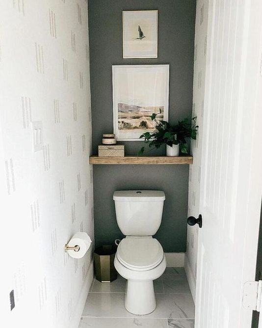 a small under the stairs powder room with a grey accent wall, a wooden shelf with decor and a toilet plus a marble tile floor