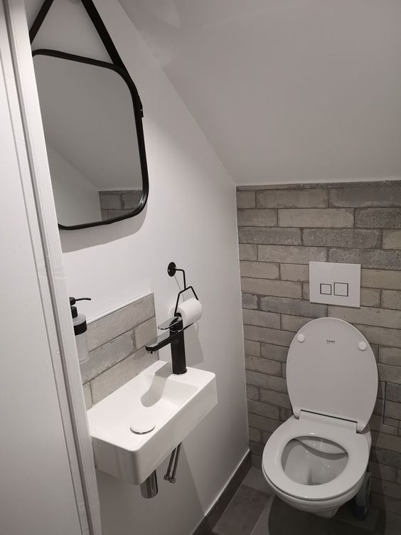 a small under the stairs powder room with brick clad imitation, a small wall-mounted sink and a mirror with rounded corners