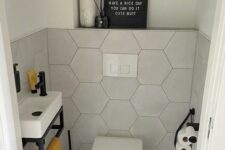 a small under the stairs powder room with hexagon tiles, a wall-mounted sink and a toilet, a shelf with some lovely decor