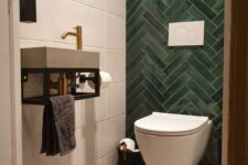 a small under the stairs powder room with white and green tiles, a concrete floor, a wall-mounted sink and a small mirror feels very modern