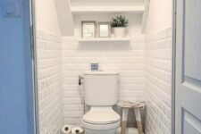 a small under the stairs powder room with white subway and printed tiles, an open shelf, some decor and a stool