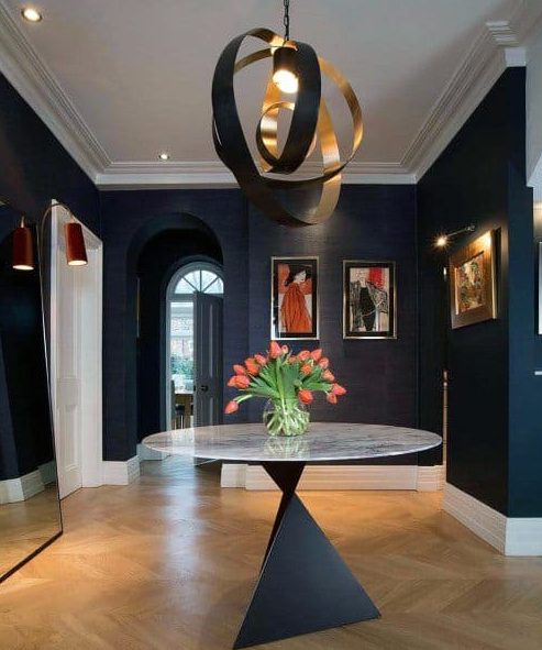a sophisticated and luxurious entryway done in black and white, with crown molding, with a fantastic black and gold chandelier, artworks and a sculptural coffee table with blooms is wow