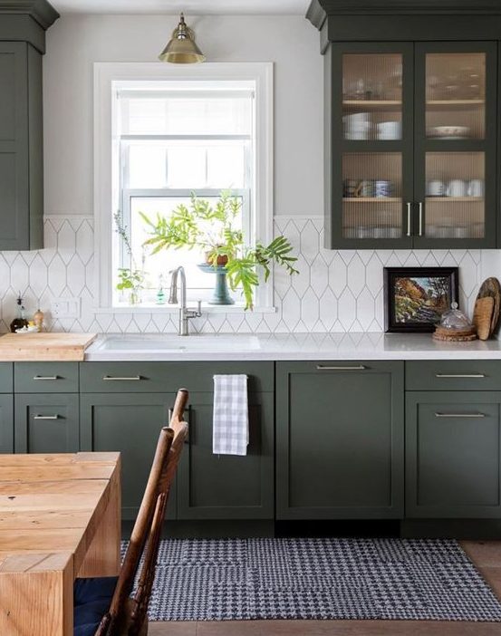 a stylish dark green kitchen with shaker cabinets, white countertops and a white tile backsplash plus retro lamps
