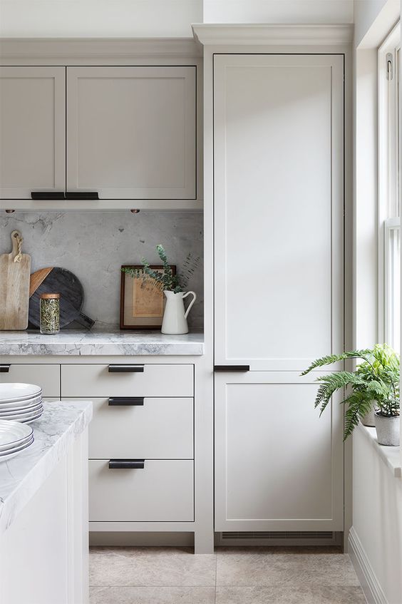 a super contemporary creamy kitchen with shaker and usual cabinets, modern black handles and a white marble backsplash and countertops