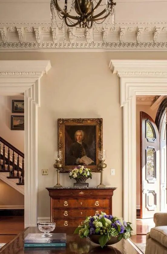 a super refined space with oversized ornated crown molding, a crystal chandelier, molding covering the doorways and vintage furniture