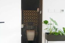 a tiny black powder room under the stairs clad with skinny and herringbone tiles, a wall-mounted toilet and a sink is a great idea