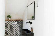 a tiny modern under the stairs pwoder room with bold tiles, a black wall-mounted sink and a catchy pendant lamp