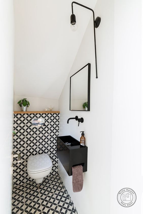 a tiny modern under the stairs pwoder room with bold tiles, a black wall-mounted sink and a catchy pendant lamp