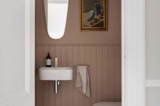 a tiny moody powder room under stairs, with mauve walls and wainscoting, white appliances and a catchy mirror is amazing