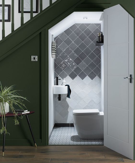 a tiny powder room under the stairs with white and grey glossy tiles, modern appliances and black fixtures