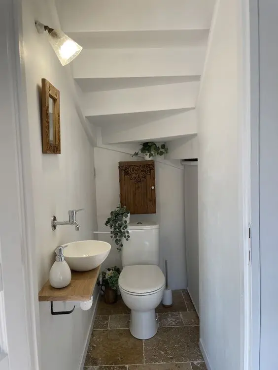 a tiny white under the stairs powder room with white appliances including a bowl sink, a stained cabinet and some greenery