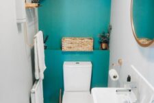a turquoise under the stairs powder room with white appliances, a radiator, some shelves, greenery and gold touches