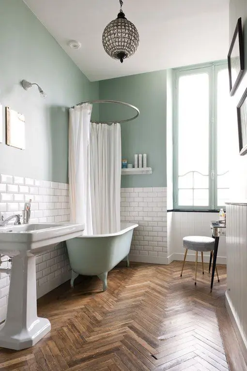 a vintage bathroom with mint green walls and a clawfoot tub, a parquet floor, vintage appliances and a lovely crystal sphere pendant lamp
