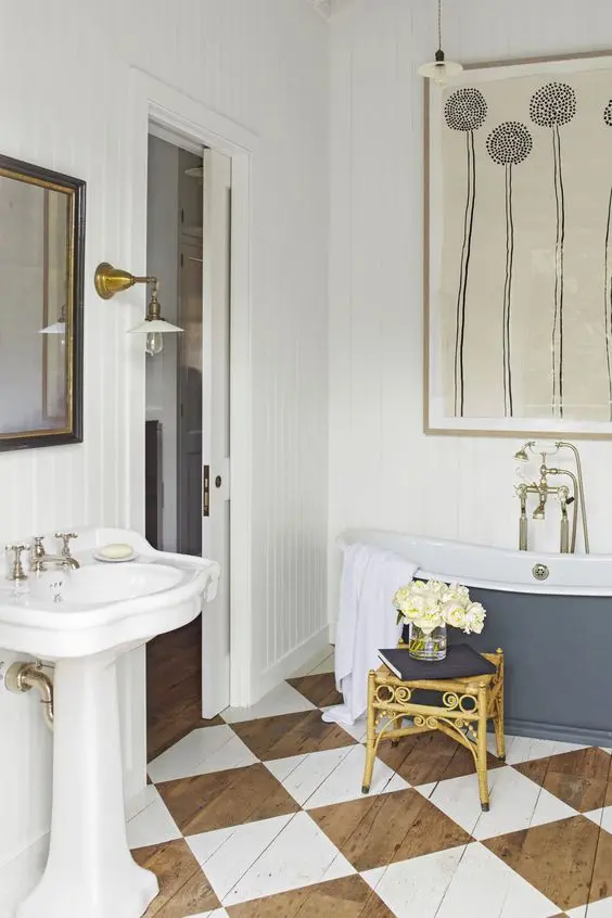 a vintage bathroom with white planked walls, a wooden floor with a geo print, a navy tub, a free-standing sink and touches of brass